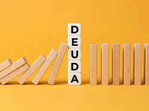 Piezas de dominó cayendo junto a la palabra deuda, representando las consecuencias del impago de un préstamo